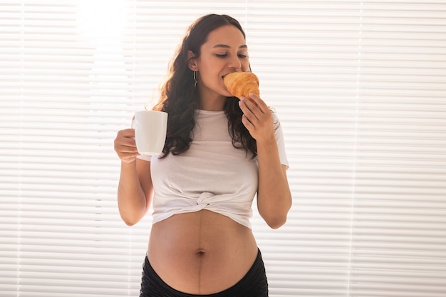 Schwangere Frau isst Croissant und trinkt Kaffee Schwangerschaft und Mutterschaftsurlaub Kopie Raum