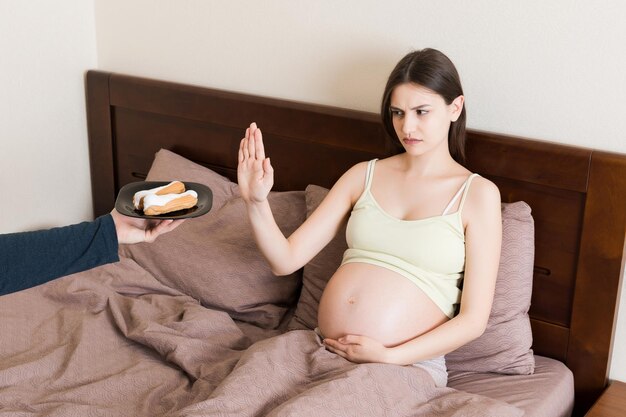 Foto schwangere frau liegt im bett und will keinen kuchen essen und macht eine haltegeste ohne süßes und dessert