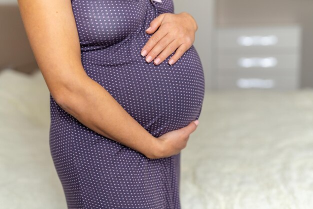 Schwangere Frau mit beiden Händen auf dem Bauch steht in ihrem Schlafzimmer Frau erwartet ein Kind in der gemütlichen Atmosphäre ihres Hauses