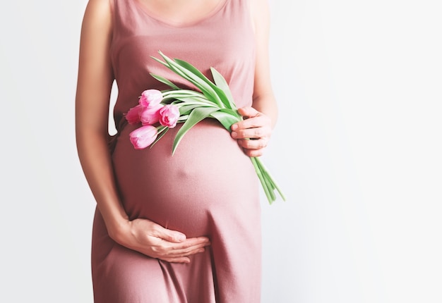 Schwangere Frau mit Blumen hält die Hände am Bauch Schwangerschaft Mutterschaft Muttertag Urlaub