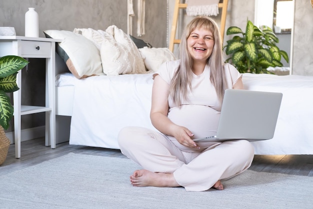 schwangere frau mit dickem bauch fortgeschrittene schwangerschaft mit laptop auf dem boden sitzend