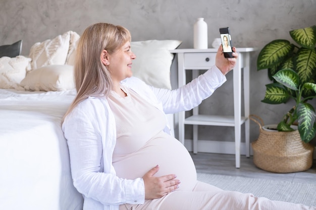 schwangere frau mit dickem bauch fortgeschrittene schwangerschaft mit telefon, das selfie macht, videoanruf hat