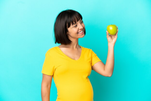 Schwangere Frau mit einem Apfel auf blauem Hintergrund isoliert auf der Suche nach Seite
