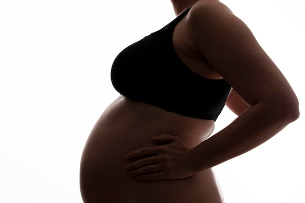 Schwangere Frau mit einem Babybauch, der auf einem weißen Hintergrund abhebt