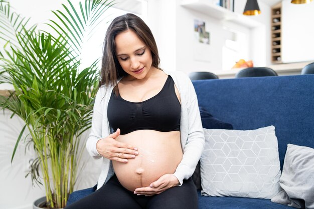 Schwangere Frau mit Feuchtigkeitscreme Frau befeuchtet ihren Bauchjunges schwangeres Mädchen reibt Sahne in ihn