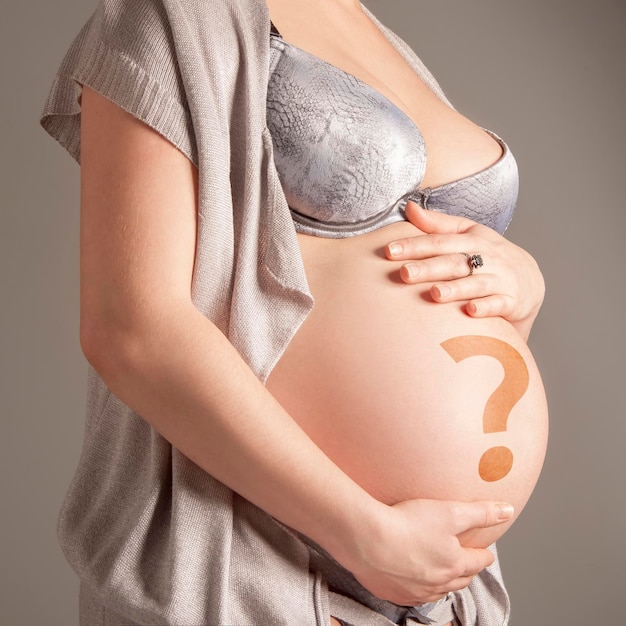 Schwangere Frau mit Fragezeichen auf ihrem Bauch