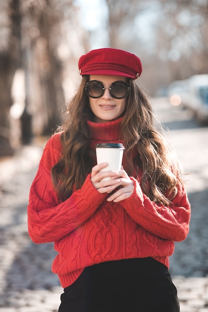 Schwangere Frau mit gestrickter Strickmütze und Sonnenbrille, die Kaffee trinkt