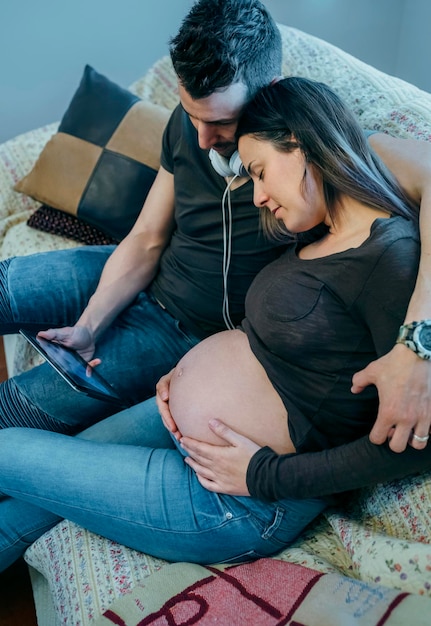 Schwangere Frau mit ihrem Partner, die auf dem Tablet einen Ultraschall ihres Babys im Wohnzimmer betrachtet