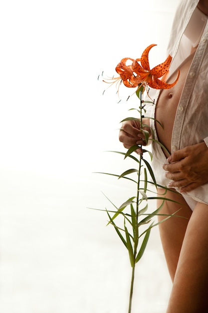 Schwangere Frau mit Lilien isoliert auf weiss. Schwangerschaftsbauch mit Blume und weißem Hemd