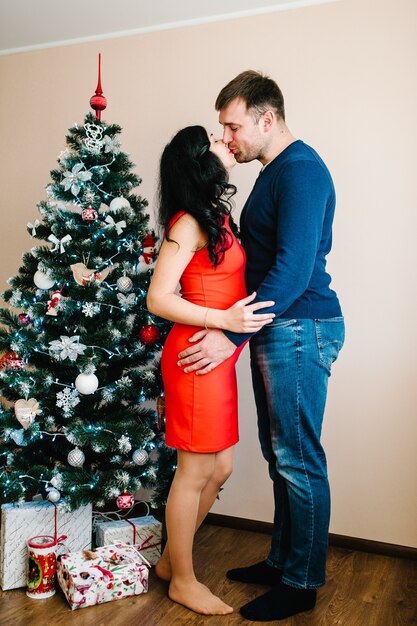 Schwangere Frau mit Mann nahe Weihnachtsbaum zu Hause Frohe Weihnachten