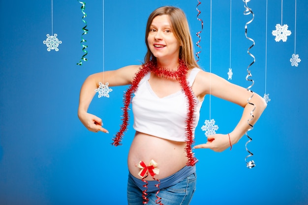 Schwangere Frau mit Schneeflocken auf blauem Hintergrund erwartet ein Baby an Heiligabend