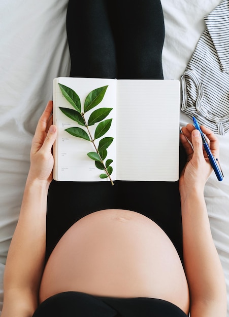 Foto schwangere frau mit schönem bauch macht notizen oder eine checkliste in einem papiertagebuch konzepte zur vorbereitung auf die geburt eines babys tipps für eine gesunde schwangerschaft minimalistische fotografie closeup in innenräumen