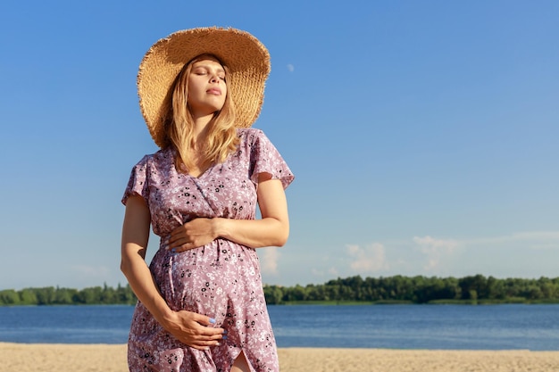 Schwangere Frau mit Strohhut am Strand