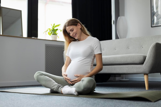 Schwangere Frau sitzt auf dem Boden und schaut auf ihren Bauch Schwangerschaftsyoga-Konzept