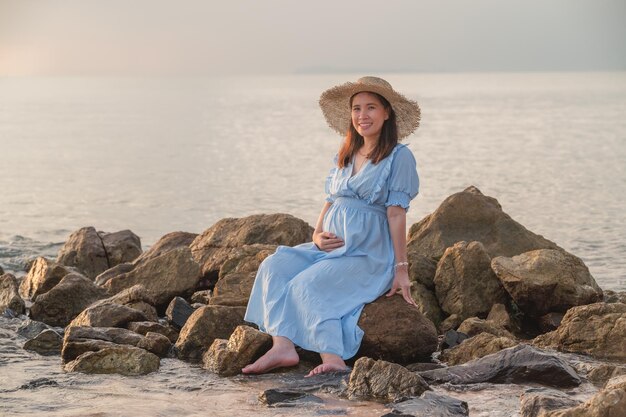 Schwangere Frau sitzt auf den Felsen nahe dem Sandstrand und dem Meer.