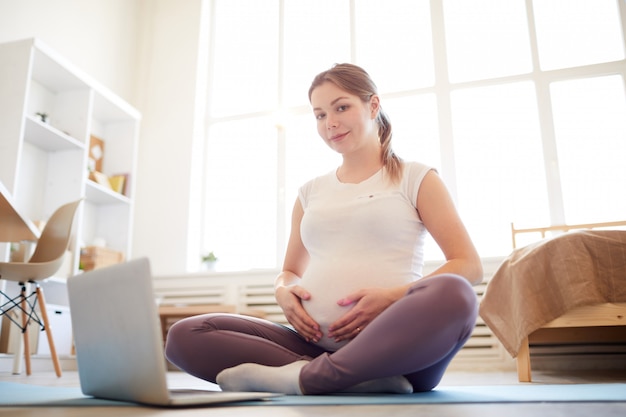 Schwangere Frau sitzt auf Yogamatte