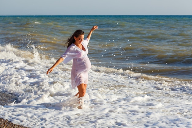 Schwangere Frau springt am Strand Fröhliche schwangere Frau läuft am Meer