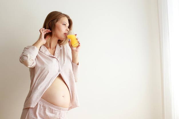 Schwangere Frau trinkt Orangensaft am Fenster