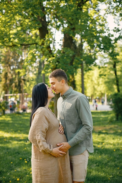 Schwangere Frau und ihr Ehemann stehen in einem Park auf einem Gras und umarmen sich