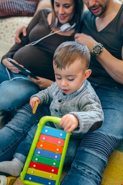 Schwangere Frau und ihr Mann schauen auf das Tablet, während ihr kleiner Sohn spielt