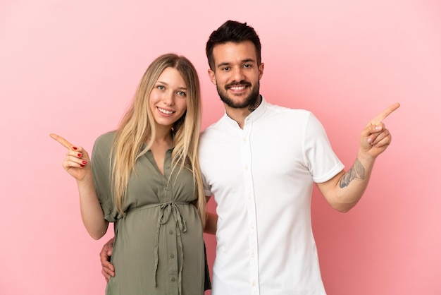 Schwangere Frau und Mann über isoliertem rosa Hintergrund, die mit dem Finger auf beide Seiten zeigen