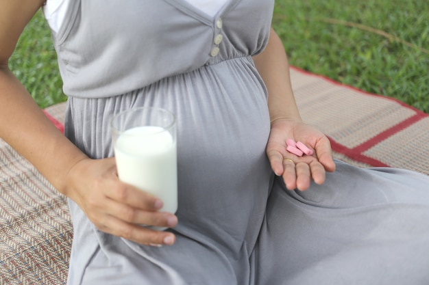 Schwangere Frauen haben ein Glas Milch und Vitaminpille in der Hand, um zu essen.