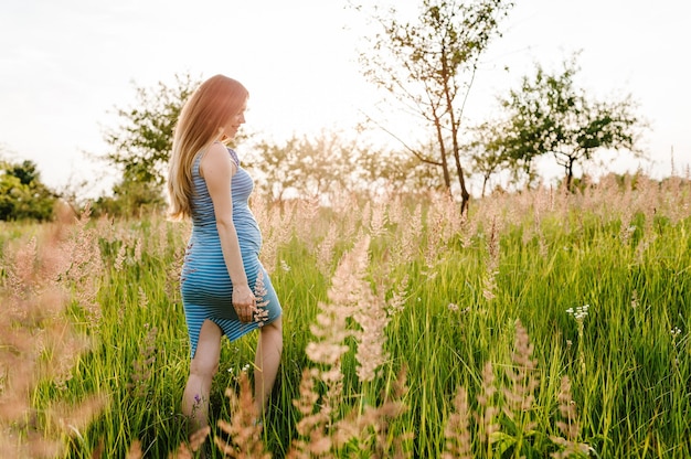 Schwangere glückliche mädchen gehen, mit rundem bauch, gehen auf gras im freien in der gartenoberfläche mit bäumen