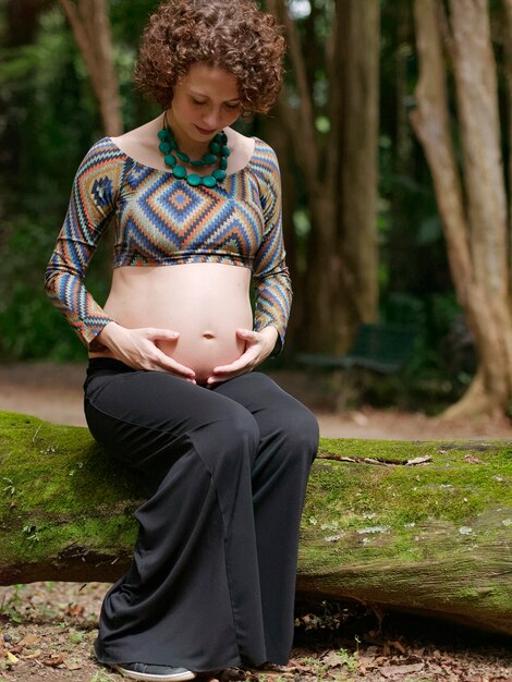 Schwangere moderne junge Frau, die draußen ihren Bauch berührt.