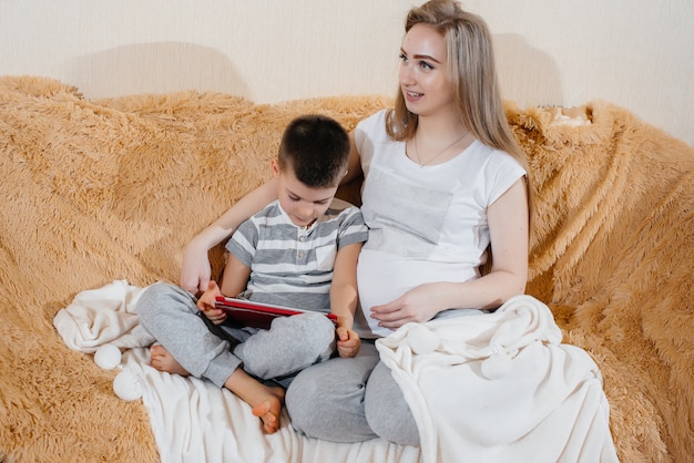 Schwangere Mutter spielt mit ihrem Sohn auf der Couch in der Tablette.