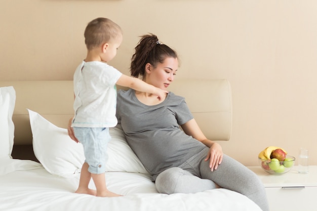 Schwangere Mutter und ihr kleiner Sohn verbringen gemeinsam Zeit zu Hause im Bett