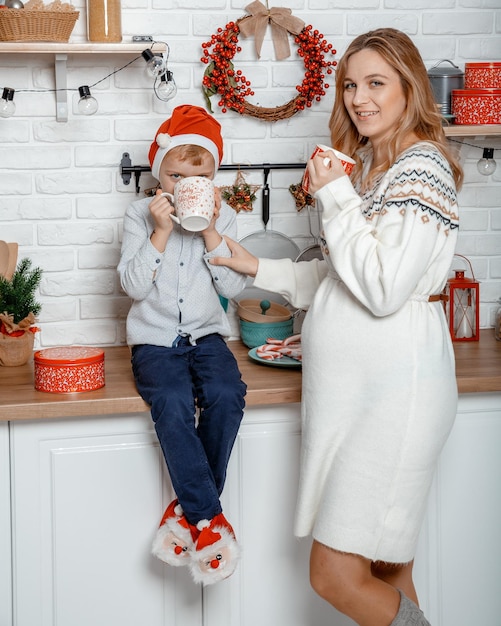 Schwangere Mutter und ihr Sohn genießen in der Küche und in der Weihnachtszeit. Schwangere Frau mit Sohn an den Neujahrsfeiertagen.