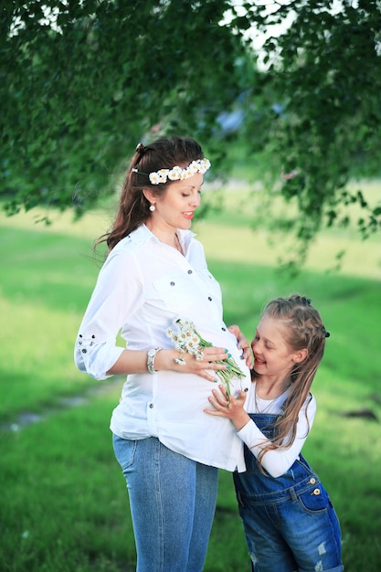 Schwangere Mutter und ihre kleine Tochter bei einem Spaziergang im Park an einem sonnigen Tag