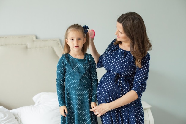 Schwangere Mutter und kleine Tochter Mutter, die Kindmädchen kämmt