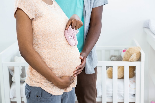 Schwangere Paare, die rosa Babyschuhe auf Frauenmagen halten