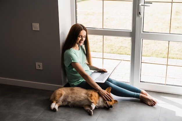 Schwangere Programmiererin, die online arbeitet und eine Pause einlegt, um ihren Hund zu umarmen. Spaß mit Welsh Corgi Pembroke