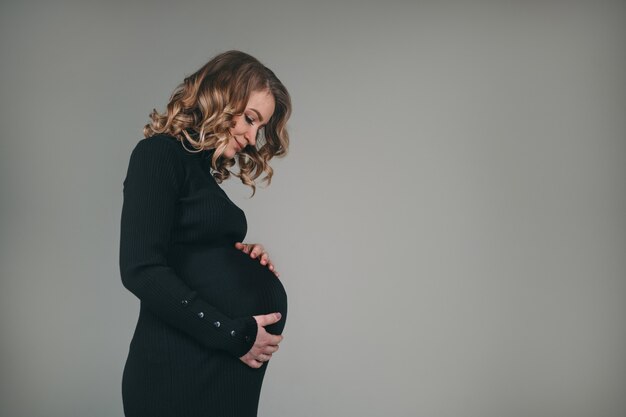 Schwangere schöne Mädchen in einem schwarzen Kleid. Eine Frau erwartet die Geburt eines Kindes.