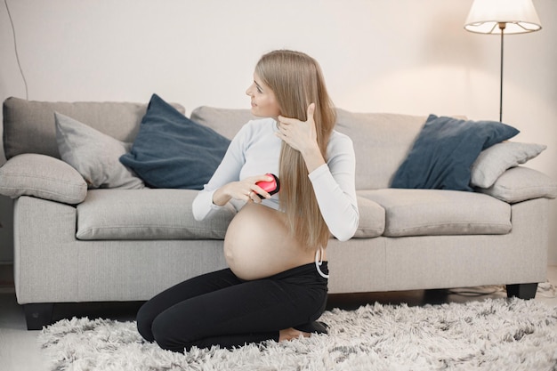 Schwangere sitzt neben einem Sofa im Wohnzimmer und bürstet sich die Haare