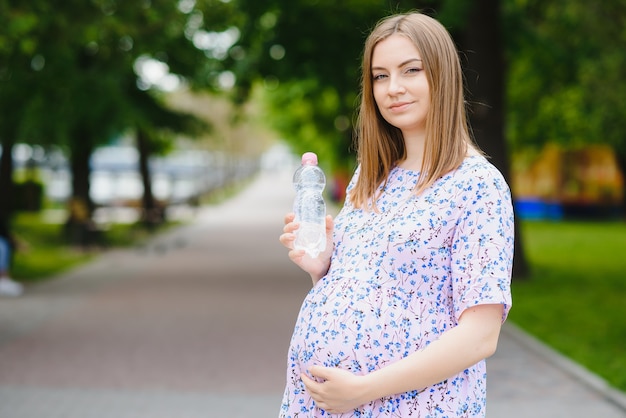 Schwangere steht im Park mit einer Flasche Wasser