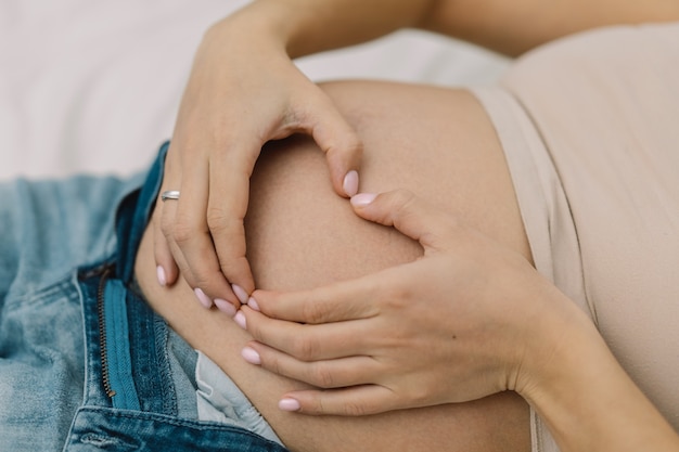Schwangere zeigt Herz auf ihrem dicken Bauch.