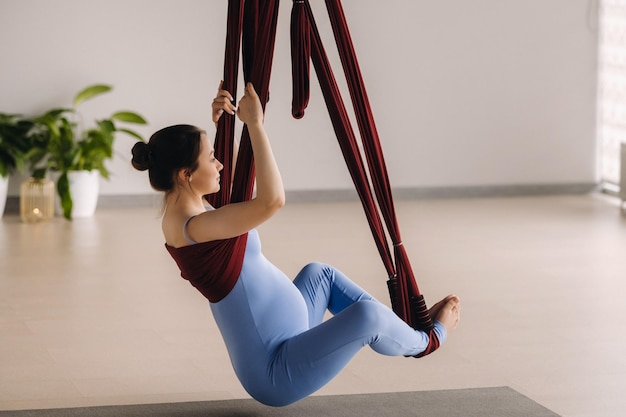 Schwangeres Mädchen Eine Frau macht Yoga auf einer Hängematte im Fitnessstudio Das Konzept eines gesunden Lebensstils Mutterschaft