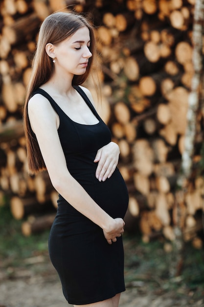 schwangeres mädchen in einem schwarzen kleid steht auf einer verschwommenen natur, der hintergrund hält ihren bauch