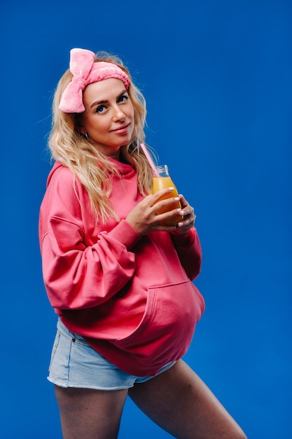 Schwangeres Mädchen in rosa Kleidung mit einer Flasche Saft auf blauem Hintergrund.