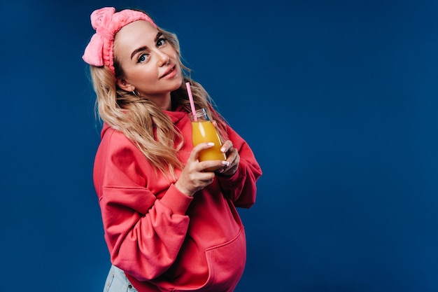 Schwangeres Mädchen in rosa Kleidung mit einer Flasche Saft auf blauem Hintergrund.