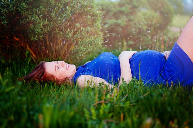 Schwangeres Mädchen legt in ein Gras und träumt von ihrer Schwangerschaft