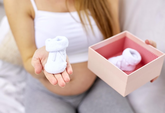 schwangerschaft, mutterschaft, menschen und erwartungskonzept - nahaufnahme einer glücklichen schwangeren frau, die zu hause eine box mit babyschuhen hält