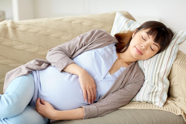 Schwangerschaft, Ruhe, Menschen und Erwartungskonzept - glückliche schwangere Frau schläft zu Hause auf dem Sofa