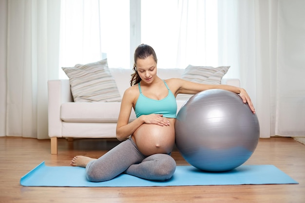 schwangerschaft, sport, fitness, menschen und gesundes lebensstilkonzept - glückliche schwangere frau, die zu hause mit fitball trainiert