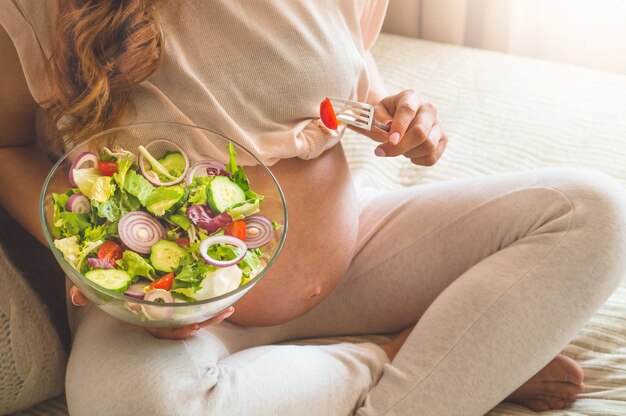 Schwangerschaft und gesunde Bio-Ernährung. Schwangere Frau, die frischen Gemüsesalat im Bett genießt, freien Raum