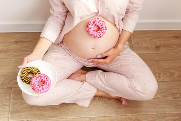 Schwangerschaft und ungesundes Ernährungskonzept Schwangere Frau mit leckeren Donuts in der Nähe