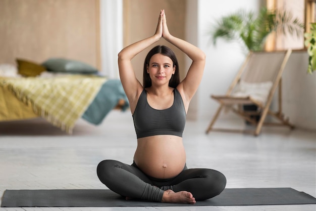 Schwangerschaft Yoga Junge schwangere Frau meditiert mit gefalteten Händen über dem Kopf